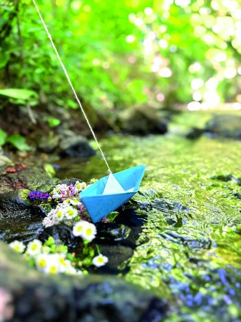 ein blaues Papierboot an einem Faden in einem Bach