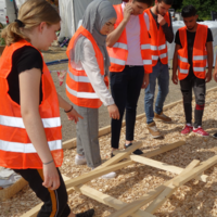 Junge Menschen mit Warnwesten und Holzteilen