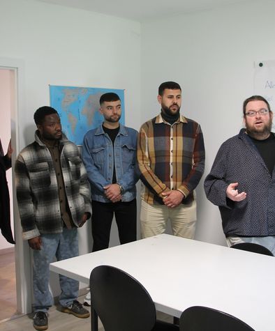 Eine Gruppe Menschen steht vor einem Tisch und spricht. 