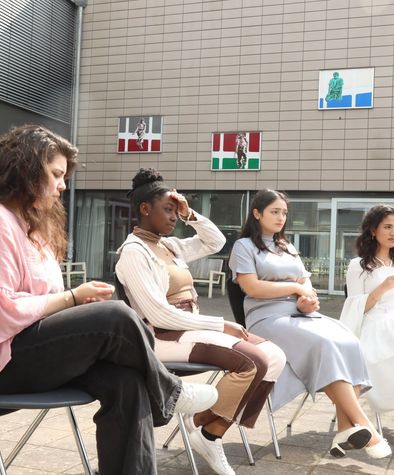 4 junge Frauen sitzen im Hof und hören zu.